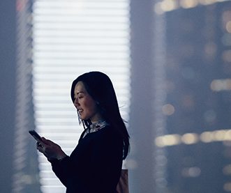 Geschäftsfrau, auf mobiles Gerät schauend, im Hintergrund Wolkenkratzer