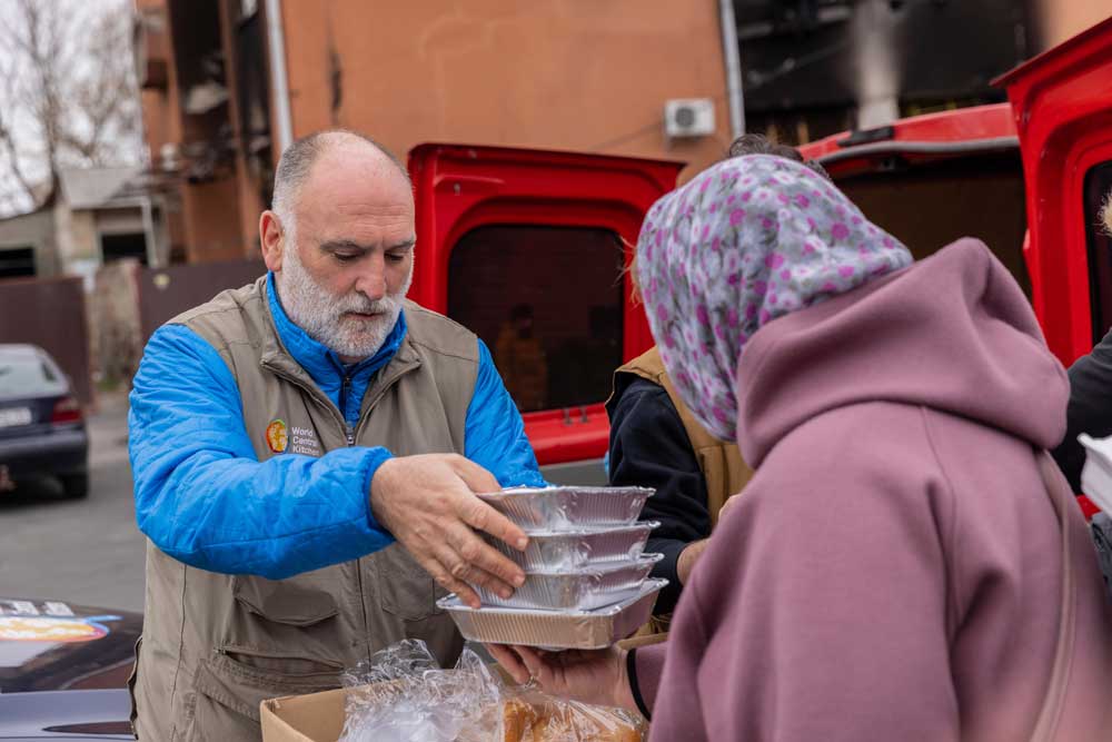 Ein WCK Mitarbeiter übergibt einer Frau mit Kopftuch vier Aluschalen mit Essen. 