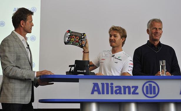 Rennfahrer Rosberg zeigt sein F1-Lenkrad und die von der Allianz gesponserte Kopfstütze.