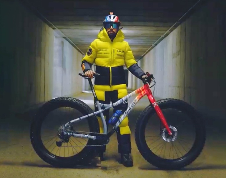 Cyclist Omar the Felice stands in a tunnel with bicycle and a big yellow jacket ready for Antarctica