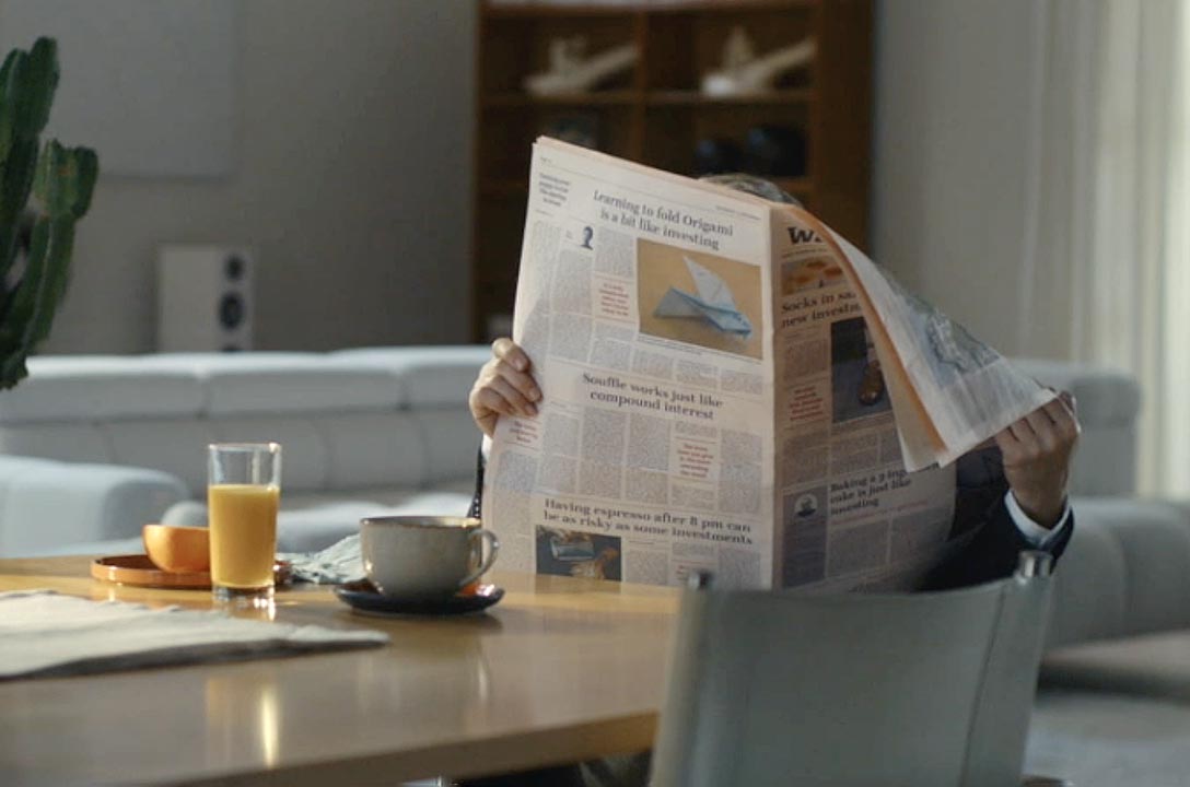 Christoph Waltz hidden behind newspaper which he is reading sitting on a table