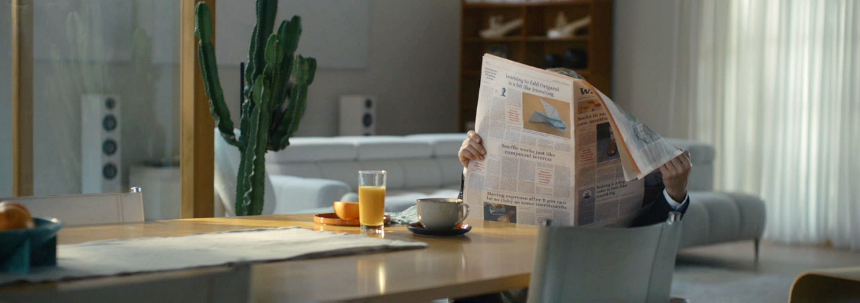 Christoph Waltz hidden behind newspaper which he is reading sitting on a table