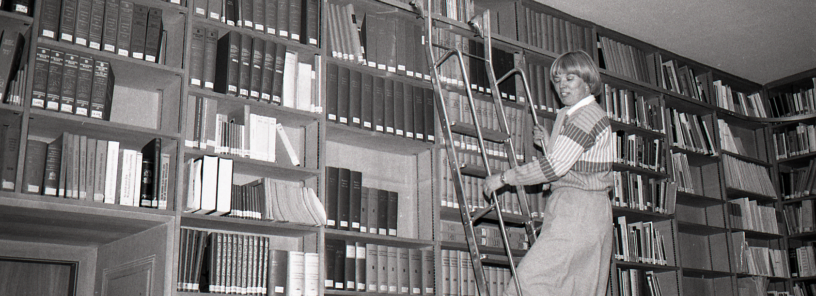 Schwarzweiß Archivfoto einer Frau an einer Leiter einer Bibliothek