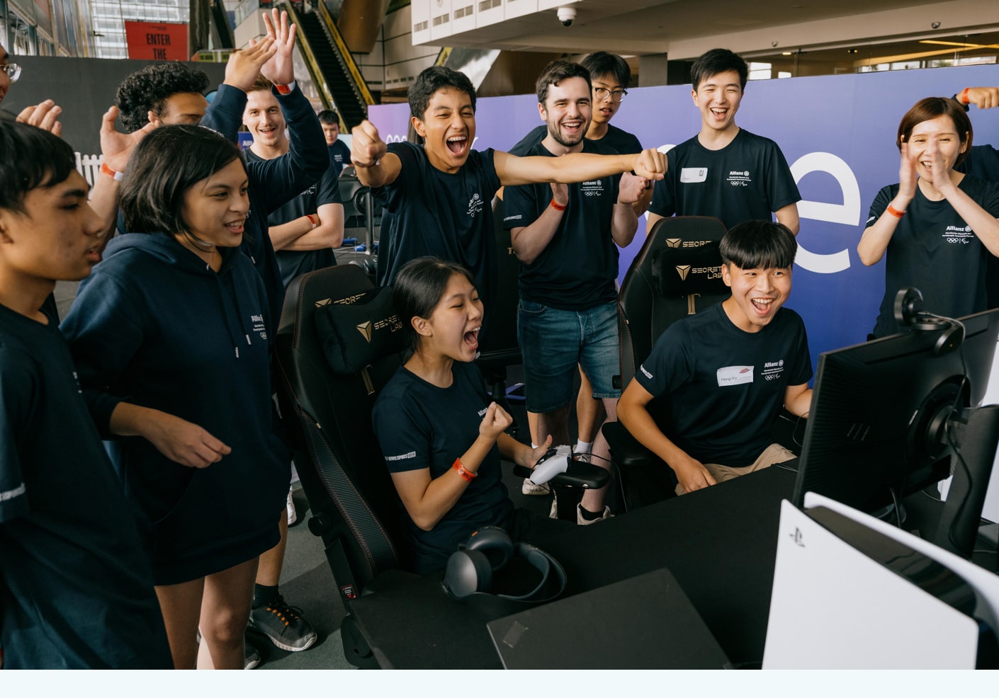 A group of young people standing around a screen and celebrating as a young woman wins a videogame competition. 