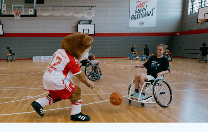 Wheelchair basketball participant playing the ball with Bernie, the Bayern mascot 