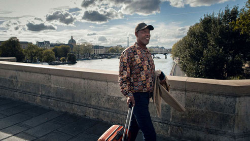 Allianz employee with a suitcase in hand, walking over a bridge in Paris with the Eiffel Tower in the background