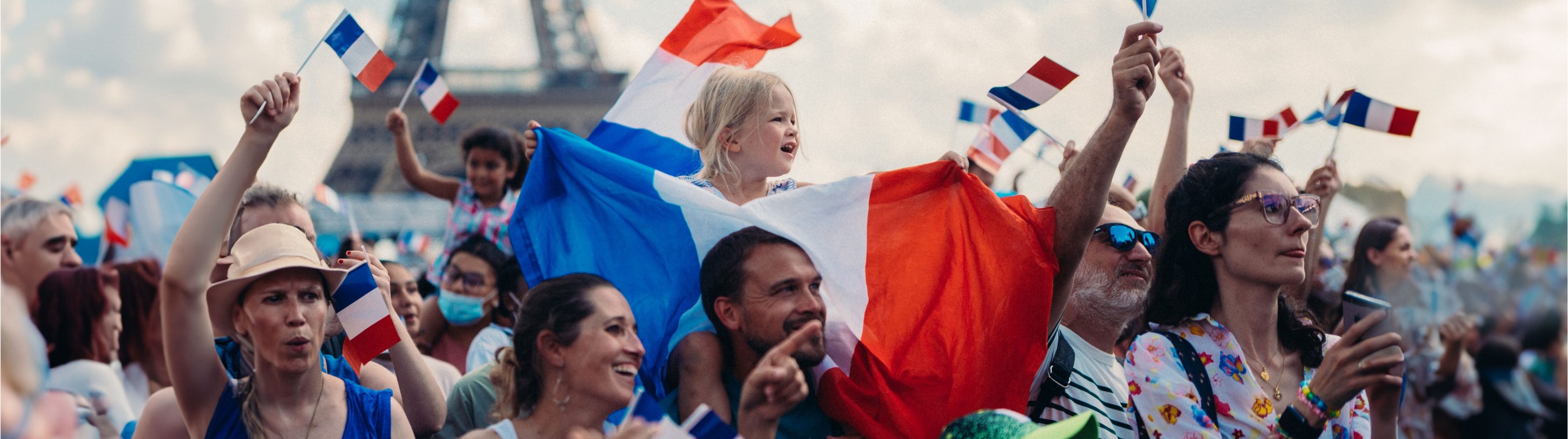 Crowd of cheering fans, girl on her father's shoulders with many waving France flags, the Eiffel Tower in the background
