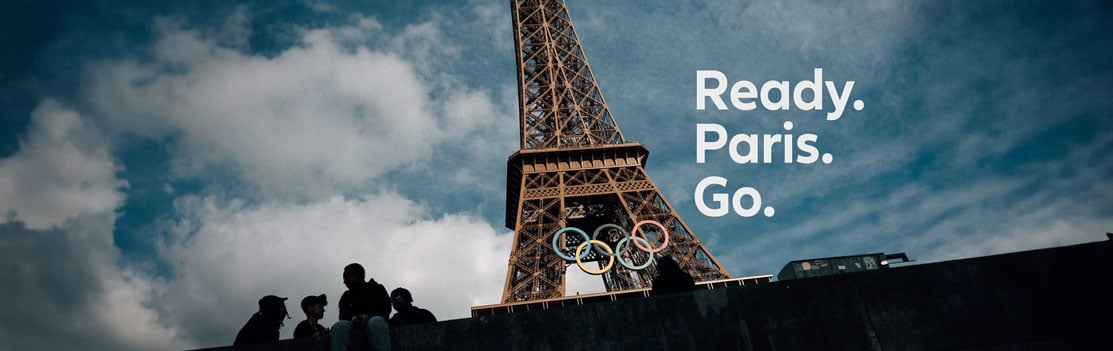 Eiffel Tower with Olympic Rings logo on it from below. Headline invites you to the Olympic and Paralympic Games: Paris. Ready. Go.