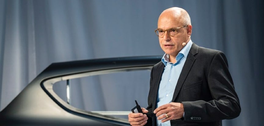 A presenter gives a talk standing in front of a car's body parts