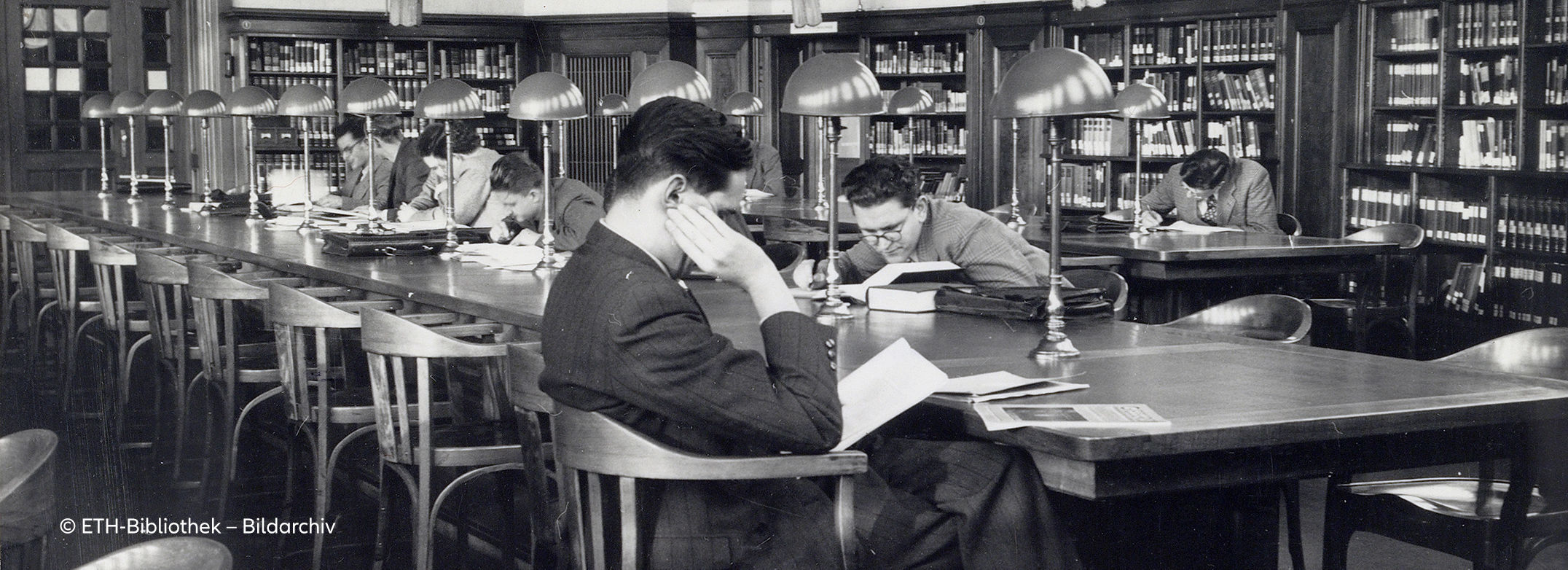 Black and white archive photo of young men sitting at a long table in a library. Copyright: ETH Library Image Archive